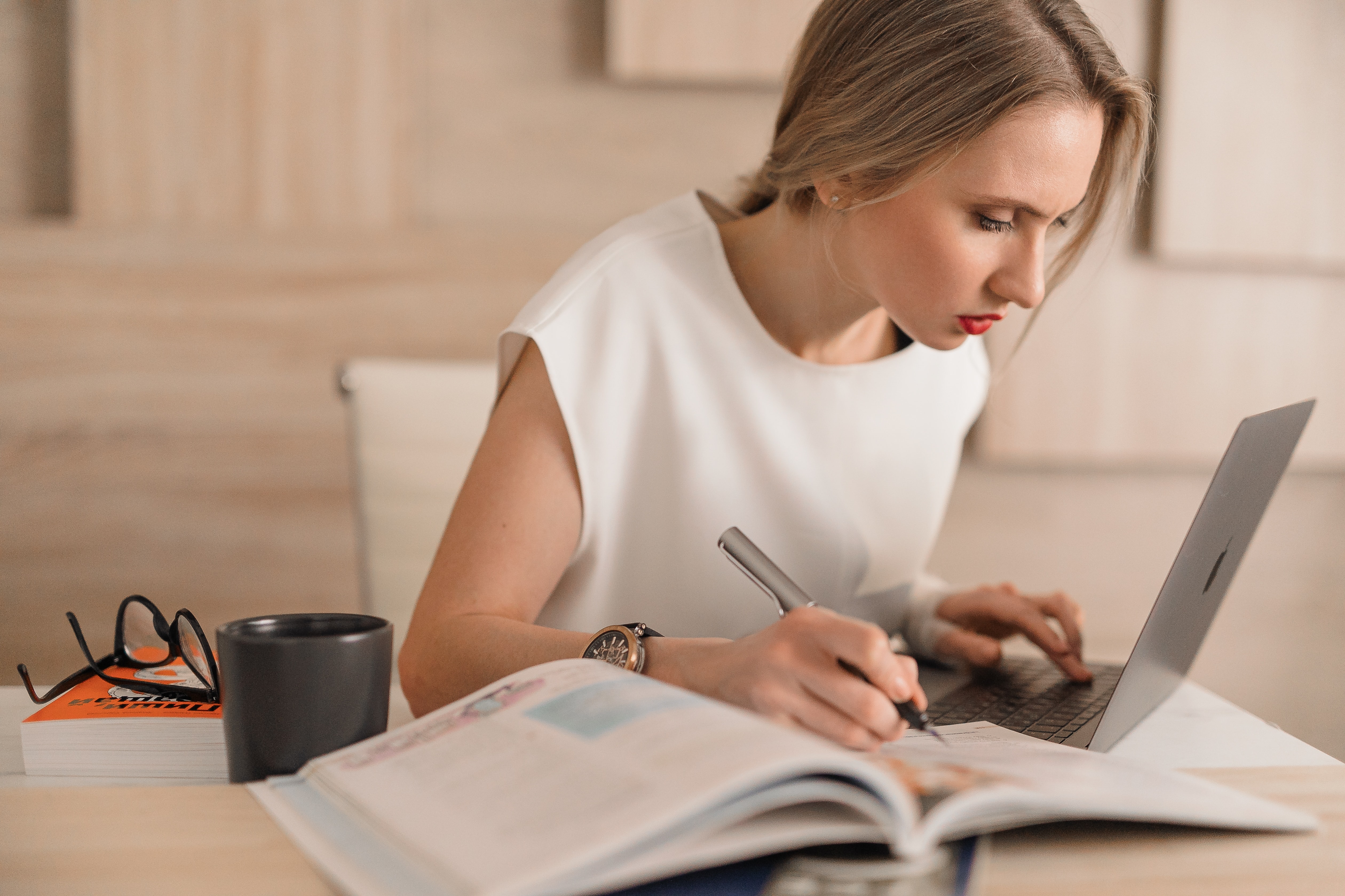 Woman working diligently on a computer while referencing a book.